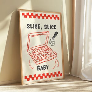 A framed print with a red and white checkered border, depicting a pizza box with a pizza inside, a pizza cutter, and the text "SLICE, SLICE BABY," leaning against a light-colored wall.