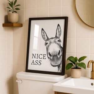 May include: A framed black and white wall art print featuring a detailed charcoal-style illustration of a donkey's face looking forward. The text NICE ASS is printed in a bold, black serif font on the left side of the white background.
