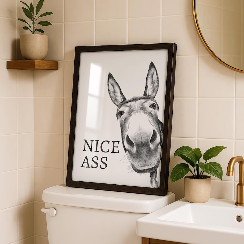 May include: A framed black and white wall art print featuring a detailed charcoal-style illustration of a donkey's face looking forward. The text NICE ASS is printed in a bold, black serif font on the left side of the white background.