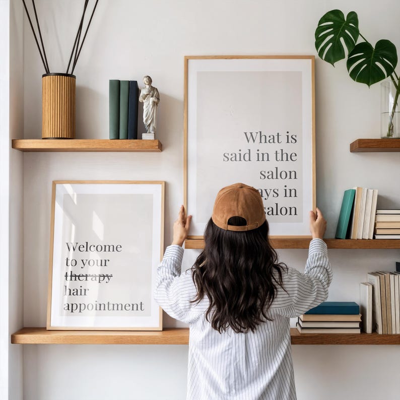 May include: Two framed wall art prints with black text on a light background. One print reads, "Welcome to your therapy hair appointment," and the other reads, "What is said in the salon stays in the salon." The prints are displayed on wooden shelves.