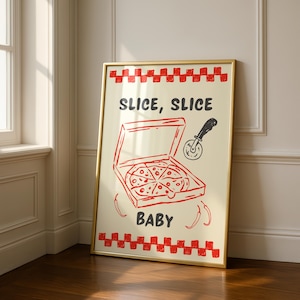 A framed print with a red and white checkered border, depicting a pizza box with a pizza inside, a pizza cutter, and the text "SLICE, SLICE BABY," leaning in a room corner on a wooden floor.