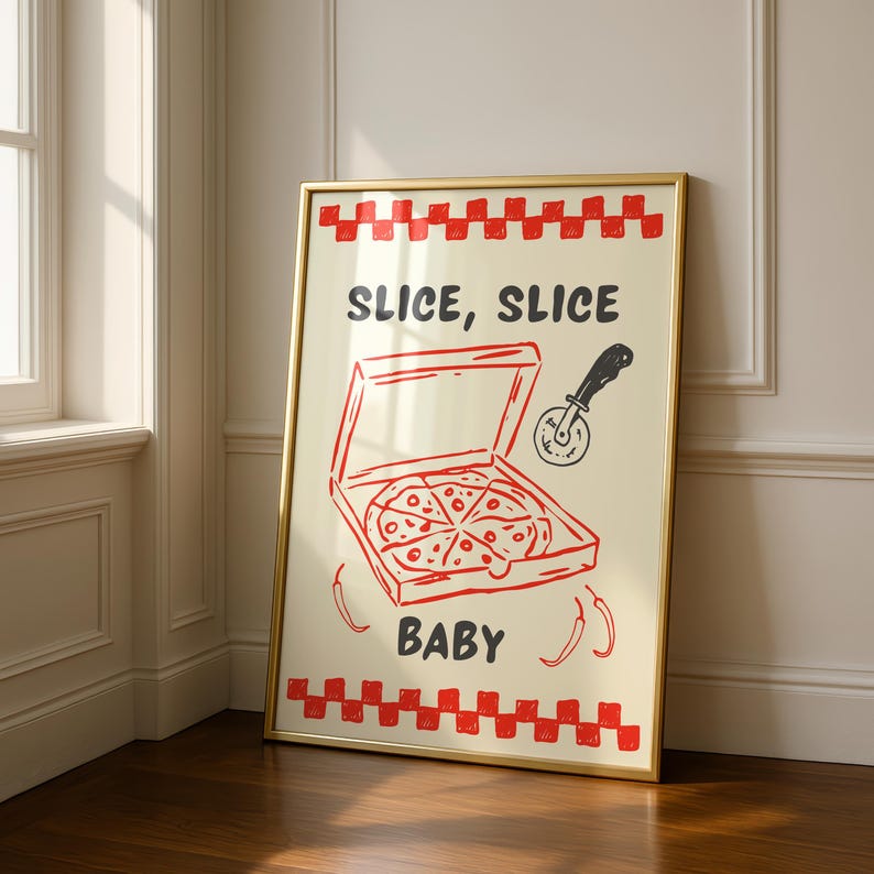 A framed print with a red and white checkered border, depicting a pizza box with a pizza inside, a pizza cutter, and the text "SLICE, SLICE BABY," leaning in a room corner on a wooden floor.