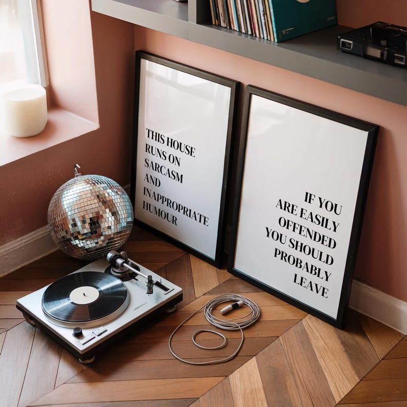 May include: Two rectangular black-framed wall art prints with white backgrounds and black text. The left print reads: THIS HOUSE RUNS ON SARCASM AND INAPPROPRIATE HUMOUR. The right print reads: IF YOU ARE EASILY OFFENDED YOU SHOULD PROBABLY LEAVE.