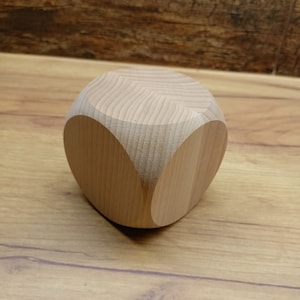 Può includere: Una forma geometrica in legno marrone chiaro con bordi arrotondati. La forma è un cubo con bordi arrotondati ed è in legno.