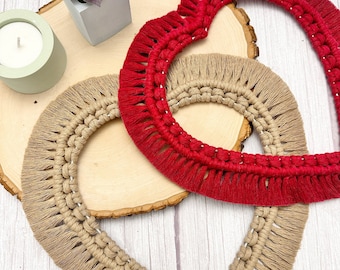 May include: Two heart-shaped macrame wall hangings, one in a natural beige color and the other in a bright red color. The hangings are made with thick yarn and have a fringe detail around the edges.