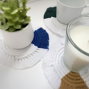 Puede incluir: Tres posavasos de ganchillo hechos a mano con flecos. Los posavasos son blancos con una sección de color diferente en cada uno. Un posavasos es blanco con una sección azul oscuro, otro es blanco con una sección verde oscuro y el último es blanco con una sección marrón.