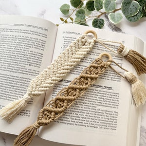 Puede incluir: Dos marcapáginas de macramé hechos a mano, uno en beige y otro en blanco, con borlas. Los marcapáginas están sobre un libro abierto con texto sobre inversión inmobiliaria.