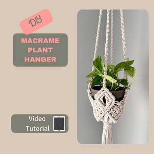 以下が含まれることがあります： 白いコードと鉢植えの植物が吊り下げられたDIYマクラメプラントハンガー。テキスト「DIY MACRAME PLANT HANGER」は緑色の背景に、テキスト「Video Tutorial」は緑色の背景に白い電話のアイコンがあります。