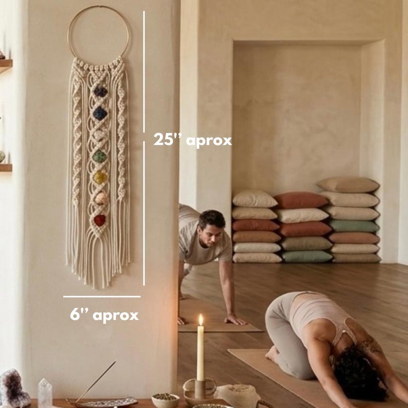 May include: A cream-colored macrame wall hanging featuring a circular gold hoop at the top and seven vertically aligned colorful gemstones in the center. The piece measures approximately 25 inches in height and 6 inches in width.