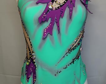 May include: A turquoise leotard with a purple and black design. The leotard is decorated with rhinestones and has a jagged edge.