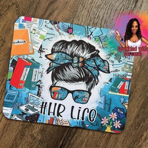 May include: A square mousepad with a cartoon illustration of a woman with sunglasses and a messy bun. The background is a light blue with office-related graphics. The text "#HR Life" is at the bottom.
