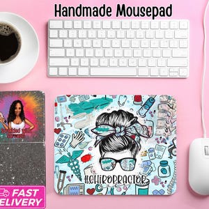 May include: A handmade mousepad with a colorful design featuring a woman's face wearing glasses, surrounded by chiropractic-related illustrations. The text "#CHIROPRACTOR" is visible. A white keyboard, mouse, and pencil are also present.