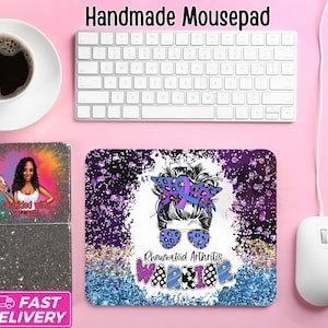 May include: A handmade mousepad with a purple and blue design featuring a woman with a messy bun, sunglasses, and a purple ribbon. The text "Rheumatoid Arthritis Warrior" is also on the mousepad. A keyboard, mouse, and pencil are also visible.