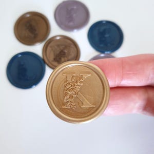 May include: Gold wax seal with a floral design and the letter K in the centre.