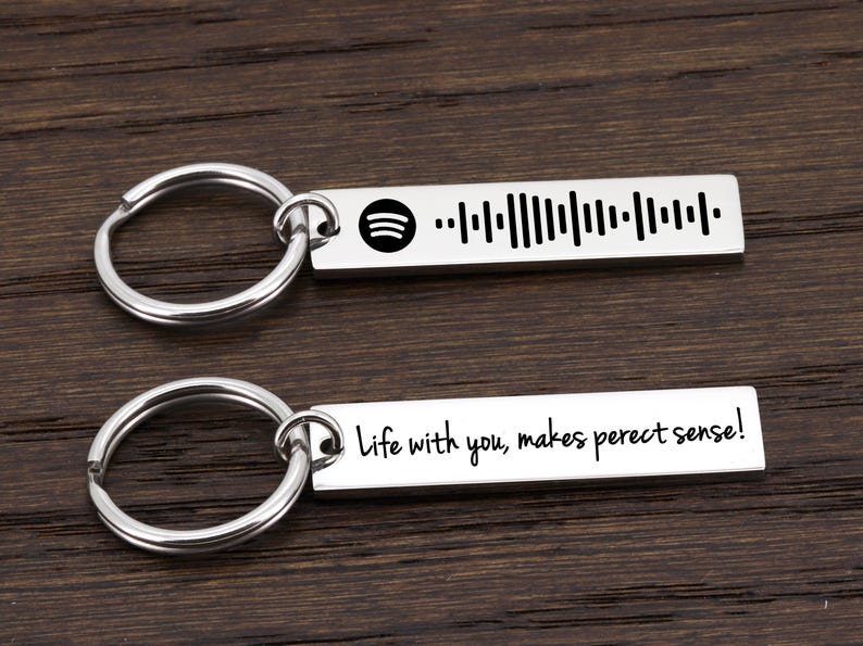 May include: Two silver keychains with a bar-shaped charm. The top charm has a barcode and the text "Life with you, makes perfect sense!" The bottom charm has a barcode and the text "Life with you, makes perfect sense!"