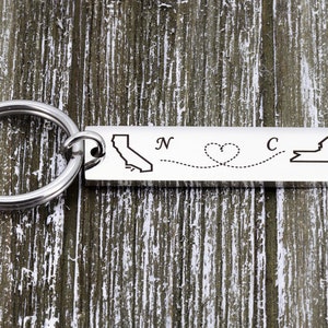 May include: Silver keychain with a map of California and New York connected by a dotted line with a heart in the middle. The text "N" and "C" are engraved on the keychain.