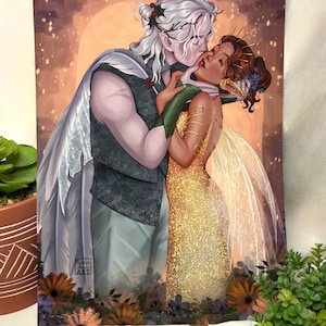 May include: An art print depicting a romantic embrace between two figures. One figure has white hair and a cape, the other wears a gold dress and floral hair accessories. The artwork uses a warm colour palette and includes floral elements.