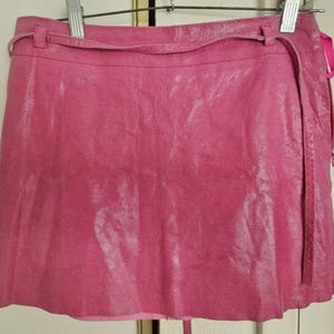 Könnte beinhalten: Ein rosa Lederrock mit einem Wickelband und einem Reißverschlussdetail. Der Rock ist kurz und hat eine glänzende Oberfläche.
