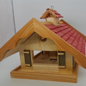 May include: Wooden birdhouse with a red shingled roof and a small overhang. The birdhouse has a small opening for birds to enter and a platform for them to perch on.