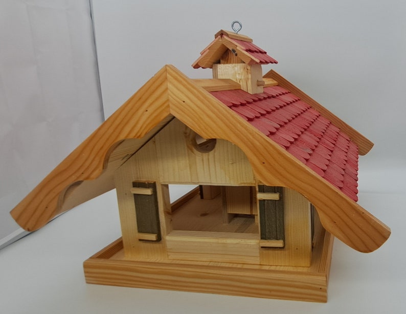 May include: Wooden birdhouse with a red shingled roof and a small overhang. The birdhouse has a small opening for birds to enter and a platform for them to perch on.