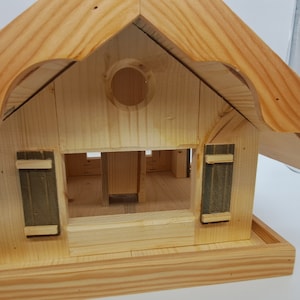 May include: Wooden birdhouse with a pitched roof and a small opening for birds to enter. The birdhouse has a small platform for birds to perch on.