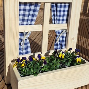 Peut inclure: Une jardinière en bois en forme de fenêtre avec des rideaux à carreaux bleus et blancs. La jardinière est remplie de plantes vertes et de fleurs violettes et jaunes.