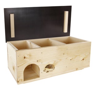 Könnte beinhalten: Ein Igelhaus aus Holz mit einem Scharnierdeckel und drei Fächern. Das Haus hat ein kleines Eingangsloch und eine eingebrannte Igel-Silhouette auf der Vorderseite.