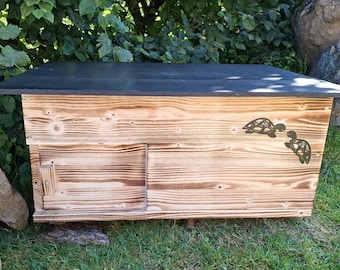 May include: A rectangular wooden enclosure with a scorched finish and a flat black top. The front panel features a small rectangular door with a vertical handle and a decorative cutout design of two sea turtles swimming toward each other.