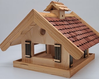 May include: Wooden bird feeder shaped like a house with a red shingled roof. The feeder has two small windows and a perch on the front.