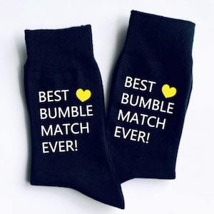 May include: A pair of black socks with white text that reads "Best Bumble Match Ever!" and a yellow heart.