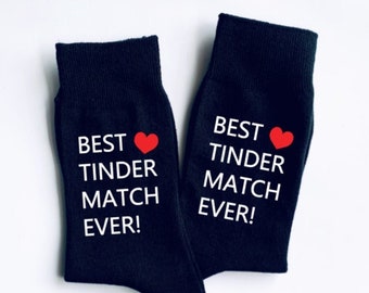 Puede incluir: Un par de calcetines negros con texto blanco que dice "Best Tinder Match Ever!" y un corazón rojo.
