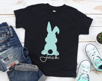 May include: Black t-shirt with a light blue bunny silhouette and the name "Jack" in cursive. The shirt is paired with blue jeans and light blue sneakers. A small potted succulent is also in the image.