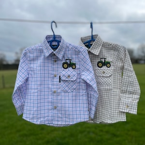 May include: Two long-sleeved plaid shirts with a tractor embroidered on the pocket. One shirt is white with blue and pink plaid, the other is white with black plaid.