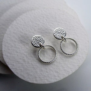 May include: Silver earrings with a textured circular disc and a twisted hoop.