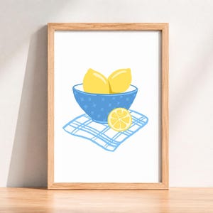 May include: A framed art print featuring a still life illustration of lemons. Two whole yellow lemons sit in a blue bowl with star-shaped designs, placed on a blue and white checkered napkin. A lemon slice rests beside the bowl.