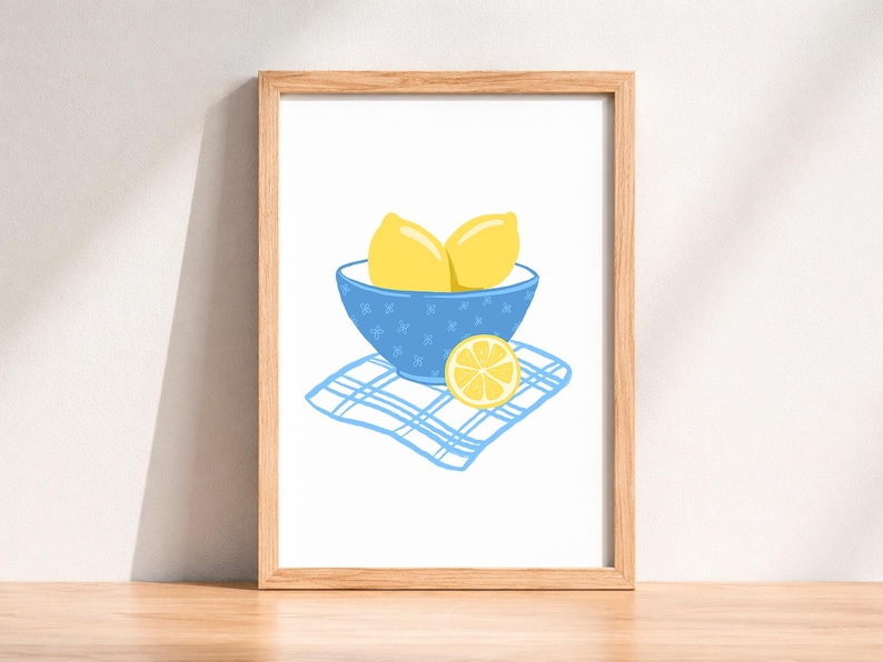 May include: A framed art print featuring a still life illustration of lemons. Two whole yellow lemons sit in a blue bowl with star-shaped designs, placed on a blue and white checkered napkin. A lemon slice rests beside the bowl.