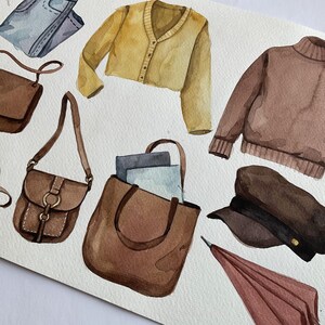 Puede incluir: Una ilustraci&oacute;n de acuarela de un atuendo de oto&ntilde;o con un su&eacute;ter marr&oacute;n, una chaqueta de punto amarilla, una bolsa de mano marr&oacute;n, una bolsa de bandolera marr&oacute;n, una gorra de marinero marr&oacute;n, un paraguas rojo y unos pantalones vaqueros azules.