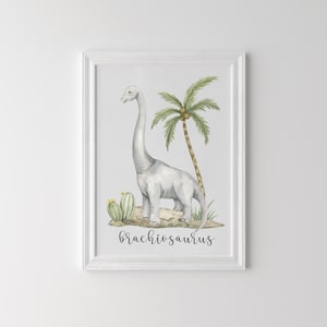 May include: Watercolor print of a Brachiosaurus dinosaur in a white frame. The artwork features a gray dinosaur, a palm tree, and cacti. The word "Brachiosaurus" is written in a cursive font at the bottom of the image.