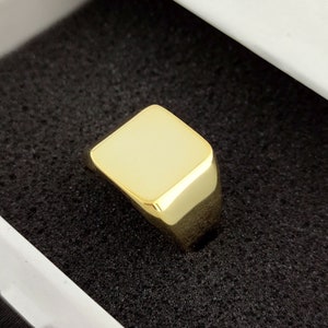 Peut inclure: Une bague signet en or avec un dessus carré. La bague est posée dans un écrin en velours noir.