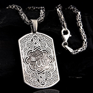 Könnte beinhalten: Eine silberne Kettenkette mit einem silbernen Anhänger mit einem komplizierten Design und dem arabischen Wort "Allah" in der Mitte.