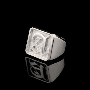 May include: A silver signet ring with a square face featuring a raised, stylized letter 'A' in a gothic font.