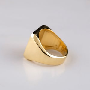 May include: A gold signet ring with a square face. The ring is made of polished gold and has a smooth, rounded band.