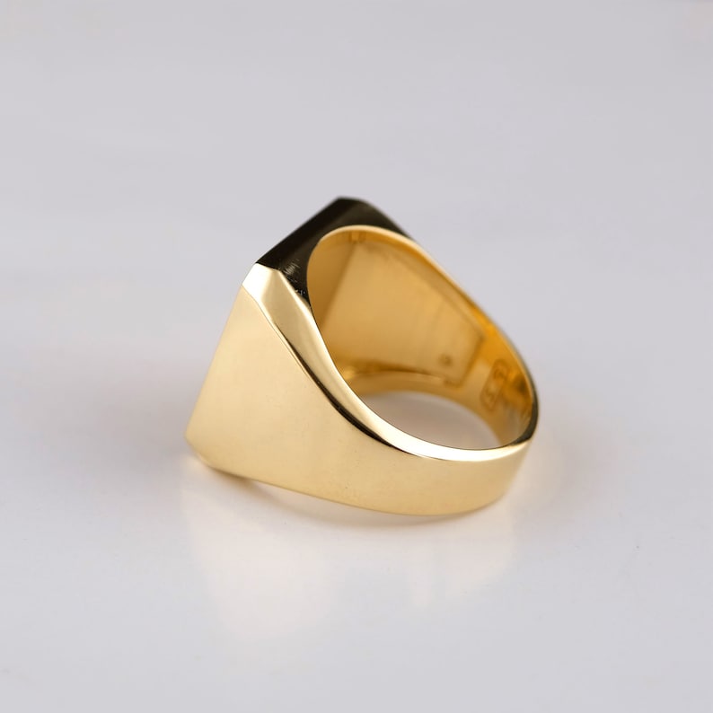 May include: A gold signet ring with a square face. The ring is made of polished gold and has a smooth, rounded band.