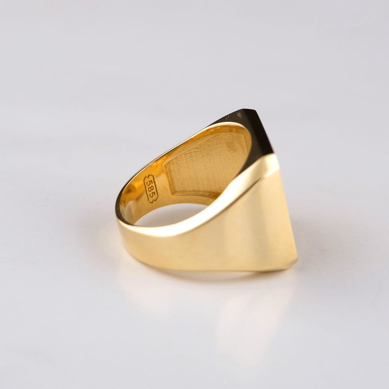 May include: A gold signet ring with a square face and a smooth, polished finish. The ring is marked with the number "585" on the inside band.