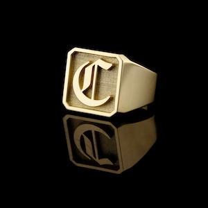 May include: A gold signet ring with a square face featuring a raised, old English letter "C".