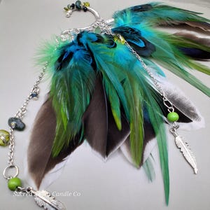 Puede incluir: Un ear cuff con plumas verdes, azules y marrones. Las plumas están unidas a un aro y cadena de metal plateado, adornados con cuentas verdes y un pequeño dije de pluma. Un diseño original y natural.