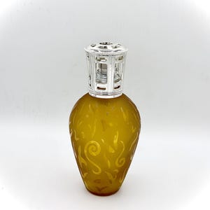 May include: A decorative amber-colored glass bottle with a silver-colored top. The bottle has a rounded shape and is adorned with a swirling, etched design. The top is a detailed, openwork design. The bottle is likely used for home fragrance or aromatherapy.