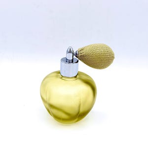 Puede incluir: Un frasco de perfume vintage con un cuerpo de vidrio amarillo-verdoso y un atomizador plateado. El atomizador tiene una pera dorada. El frasco tiene una forma redondeada con sutiles estrías verticales.