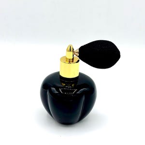 May include: A black perfume bottle with a gold-colored top and a black bulb atomizer. The bottle has a rounded shape with a ribbed design. The atomizer is made of a black, textured material.
