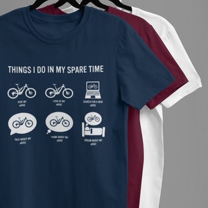 Puede incluir: Una camiseta azul marino con un gráfico blanco que dice "Things I do in my spare time" y muestra una serie de iconos que representan actividades relacionadas con bicicletas eléctricas.